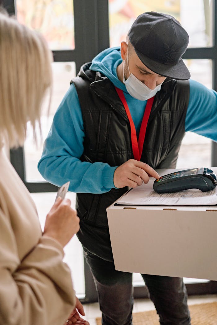 Delivery worker in mask processes contactless payment indoors with customer.